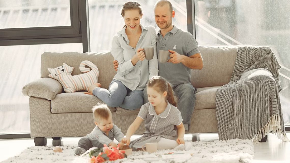 Cheerful family wearing casual clothes sitting in living room while playing and drinking tea during weekend at home in morning