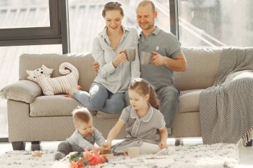Cheerful family wearing casual clothes sitting in living room while playing and drinking tea during weekend at home in morning